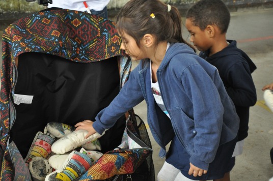 Menina deposita bonequinha de pano em mochilão, que será enviado para a Jordânia (Divulgação/Cáritas-RJ)