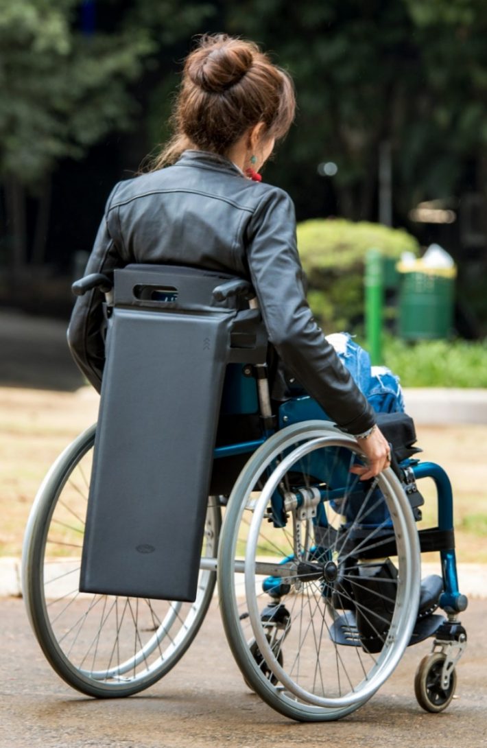 IMAGEM 02: Tapete de acessibilidade ainda não está à venda. Descrição #pracegover: Mulher em cadeira de rodas está de costas para a câmera, com o tapete de acessibilidade pendurado no encosto da cadeira. Crédito: Régis Fernandez / Ford.