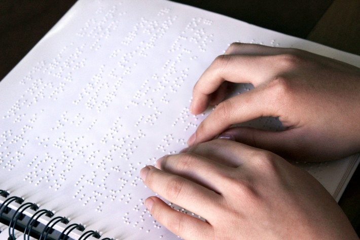 Foto mostra duas mãos de mulher sobre uma folha branca com impressão em Braille. Crédito: Divulgação.