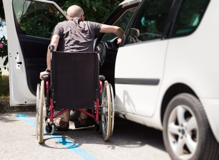 Homem em cadeira de rodas está de costas para a câmera enquanto entra em um carro branco. Crédito: Reprodução.
