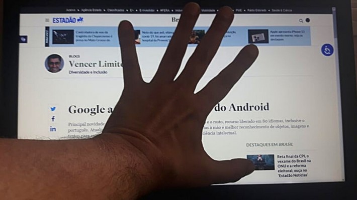 Foto da tela do blog Vencer Limites com a reportagem sobre a ampliação da acessibilidade do Android, anunciado pelo Google. No meio da tela, uma mão aberta, impedindo a leitura.