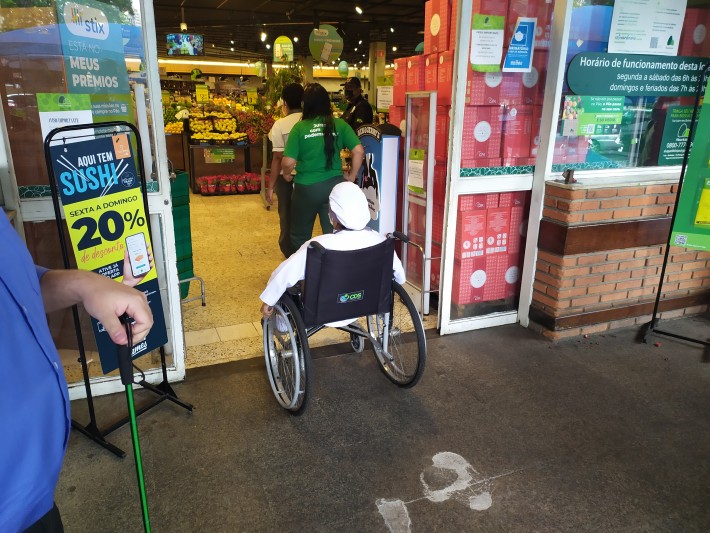 Foto de uma pessoa em cadeira de rodas entrando em um supermercado.