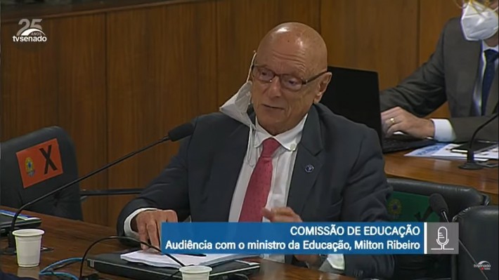 Imagem do senador Esperidião Amin falando durante sessão de comissão. Ele é um homem branco, de 73 anos, careca, de óculos, com a máscara de proteção facial pendurada na orelha, veste terno cinza, camisa branca e gravada vinho.