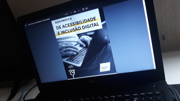 Capa do Guia Prático de Acessibilidade e Inclusão Digital na tela de um notebook. Imagem mostra foto sem cores de duas mãos sobre um teclado de computador.