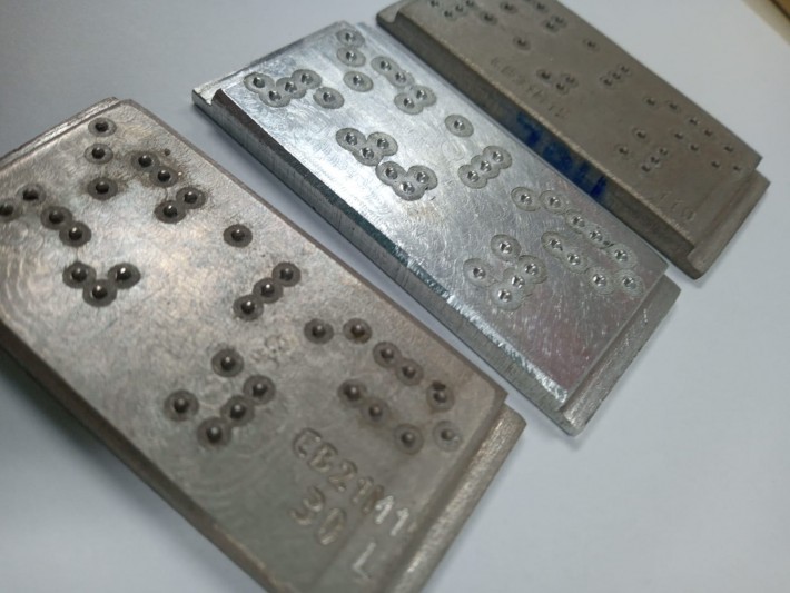 Foto das placas de alumínio com informações em braile usadas pela Embalixo.