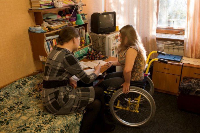 Foto de duas mulheres em um quarto. Uma das mulheres está em uma cadeira de rodas.