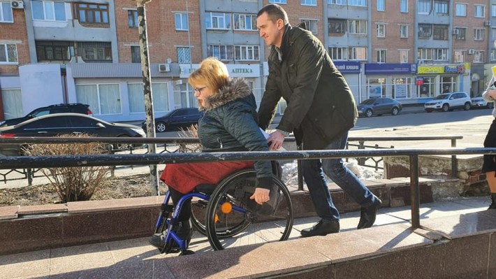 Foto de uma mulher em cadeira de rodas sendo empurrada por um homem por uma rampa em Kiev, capital da Ucrânia.