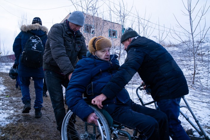 Idoso ferido é transportado em cadeira de rodas na Ucrânia.