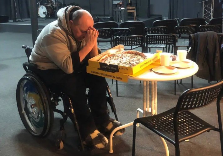 Homem em cadeira de rodas faz oração antes de comer uma pizza.