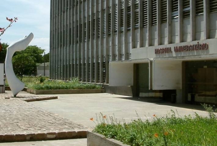 Foto da entrada do Hospital Universitário da USP, um prédio cinza com colunas de concreto nas janelas.