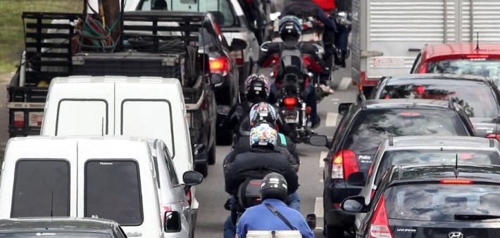 Foto horizontal de uma fileira de motos entre carros na cidade de São Paulo.