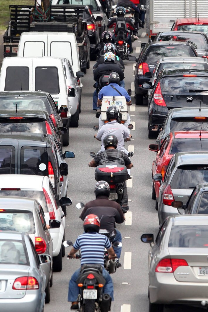 Foto vertical de uma fileira de motos entre carros na cidade de São Paulo.