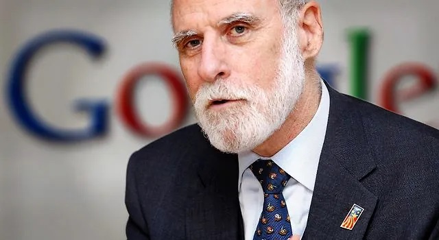 Foto de Vinton Gray Cerf, homam branco de 78 anos, careca, de barba totalmente branca. Veste terno escuro e camisa clara com gravata azul. Está falando. Ao fundo, a logomarca do Google.