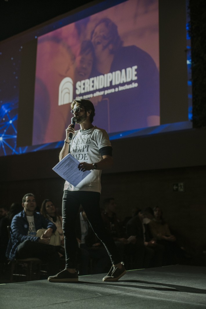Foto de Henri Zylberstajn em pé sobre um palco, falando ao microfone.