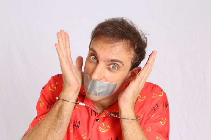 Foto do humorista Leo Lins com uma fota na boca e algemas nos pulsos.