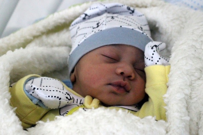 Foto do bebê Miguel com gorro colorido e roupa amarela.
